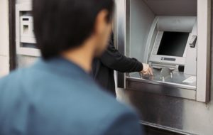 Man withdrawing cash at an ATM with a thief following him