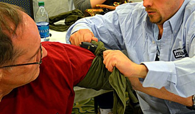 Student fashioning an improvised tourniquet with a triangular bandage and pistol magazine 