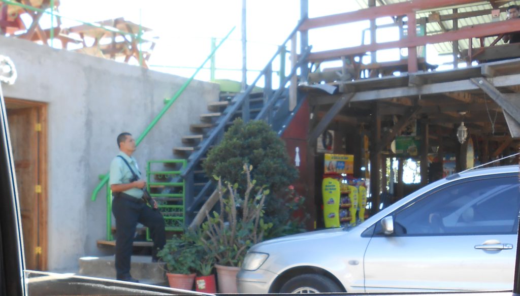 Guard carrying a slung pistol gripped shotgun outside of San Salvador restaurant.
